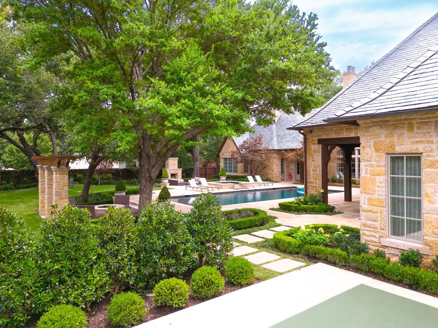 Modern residential backyard landscape design & construction with healthy trees, green plants, & a custom pool with stone construction.